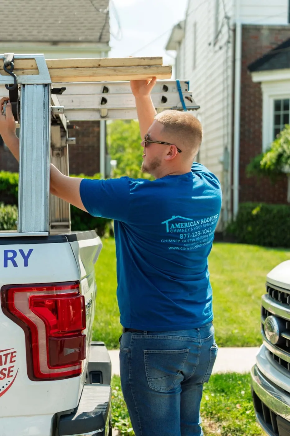 Crew member loading roofing ladders onto a company truck